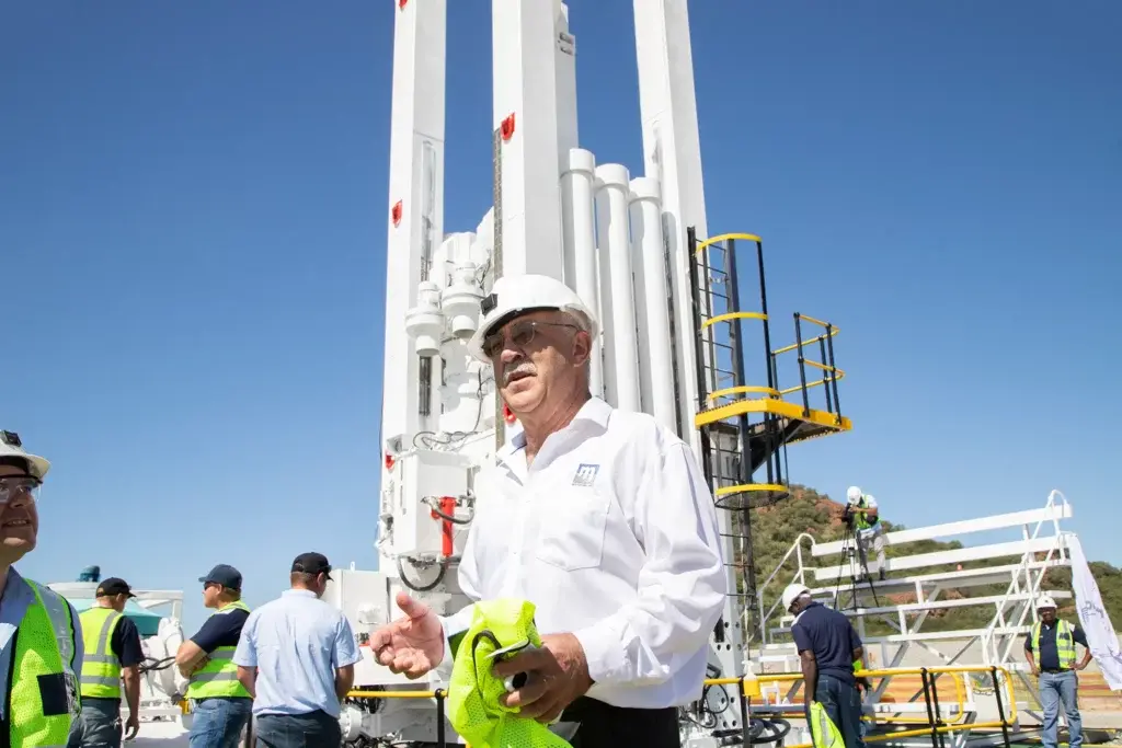 A Master Drilling leader in a white safety helmet stands with colleagues beside drilling equipment.