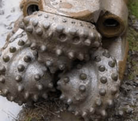 Close-up image of a pair of muddy verge mowing or mulching machine rollers with sharp, hard protrusions used for ground clearing, vegetation control, and farming. The rollers are covered with wet mud and bits of grass.