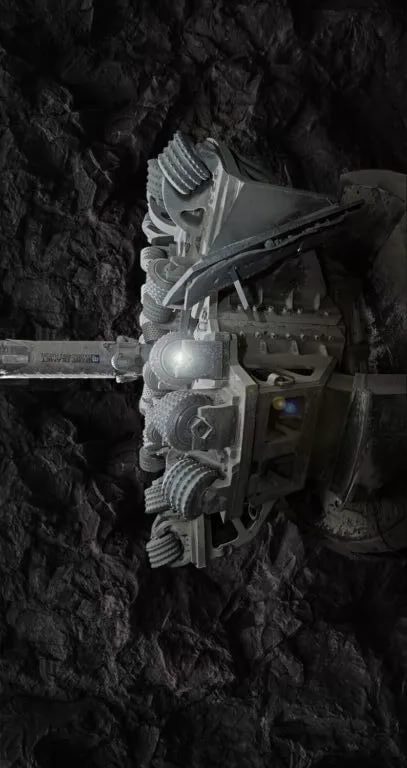 A close-up of a heavy-duty rock drilling machine with large, rotating drill bits. The machine is operating underground and is surrounded by dark, rough rock walls. The drill bits are sharp and metallic, designed for penetrating tough rock surfaces.