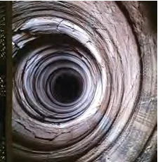 A spiraled rock formation creates the illusion of a deep, narrowing tunnel. The rock layers are curved and textured, with varying shades of brown and gray. The center appears dark, leading to a vanishing point, emphasizing the tunnel's depth.