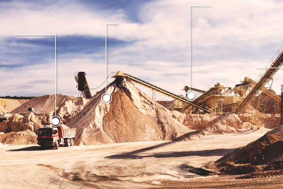 A large-scale mining operation with towering piles of excavated material. Multiple conveyor belts transport the material, and a dump truck is parked near one of the mounds. The sky is partly cloudy, indicating a clear day.